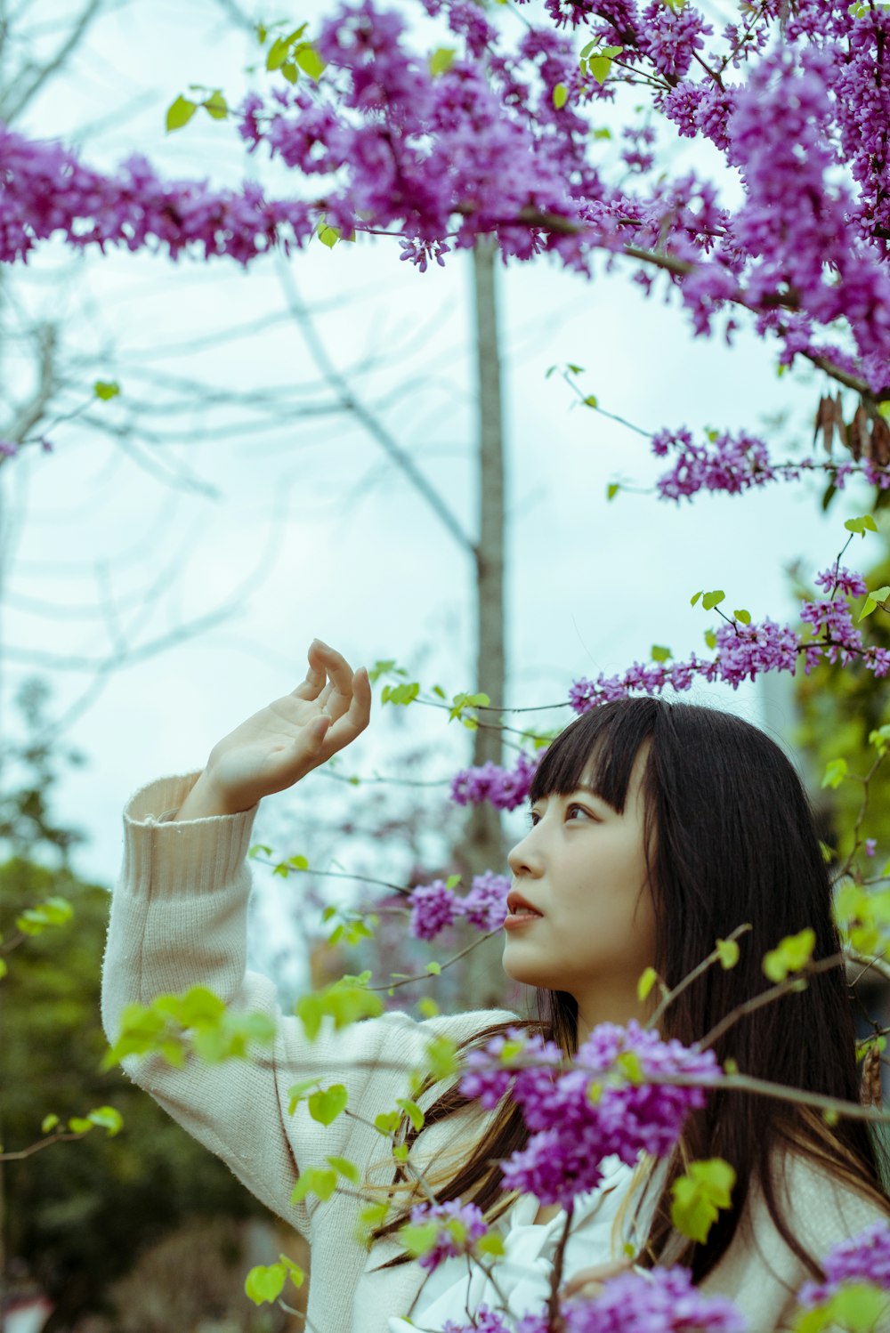 a woman standing under a tree with purple flowers