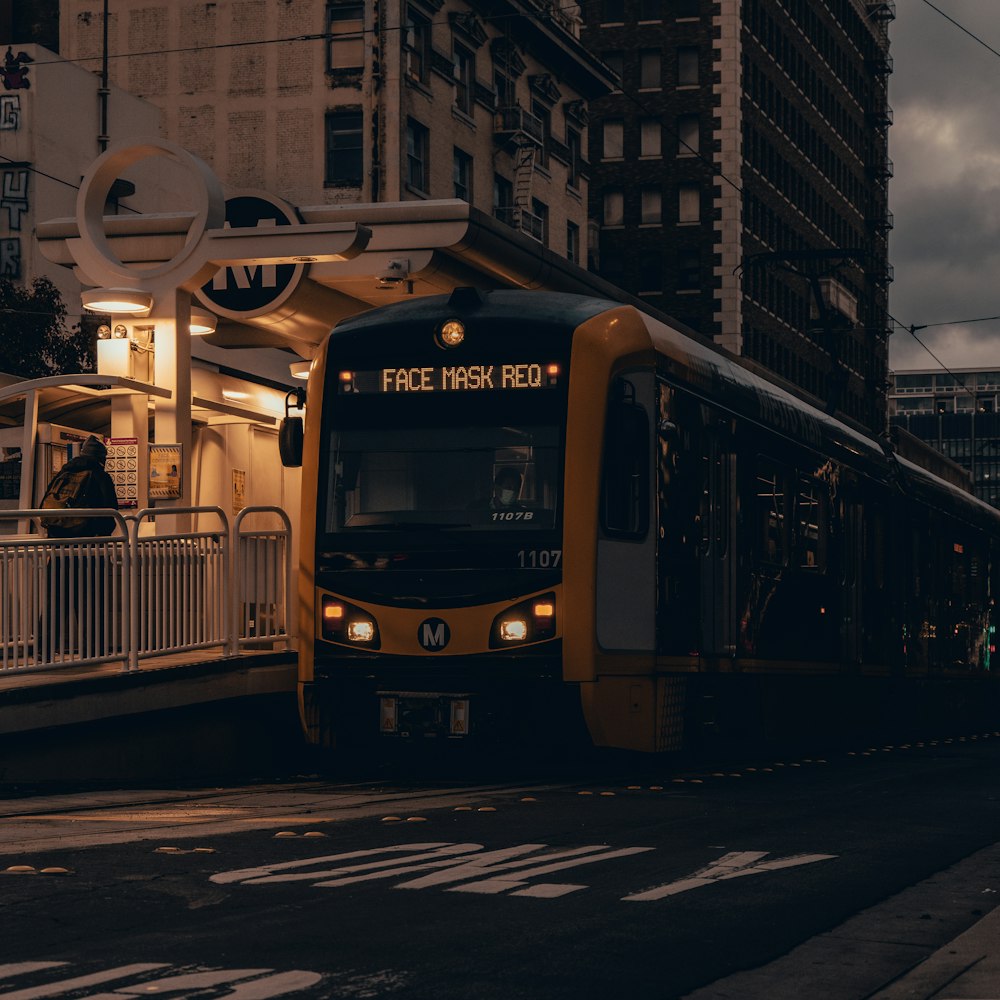 a yellow and black train traveling past tall buildings