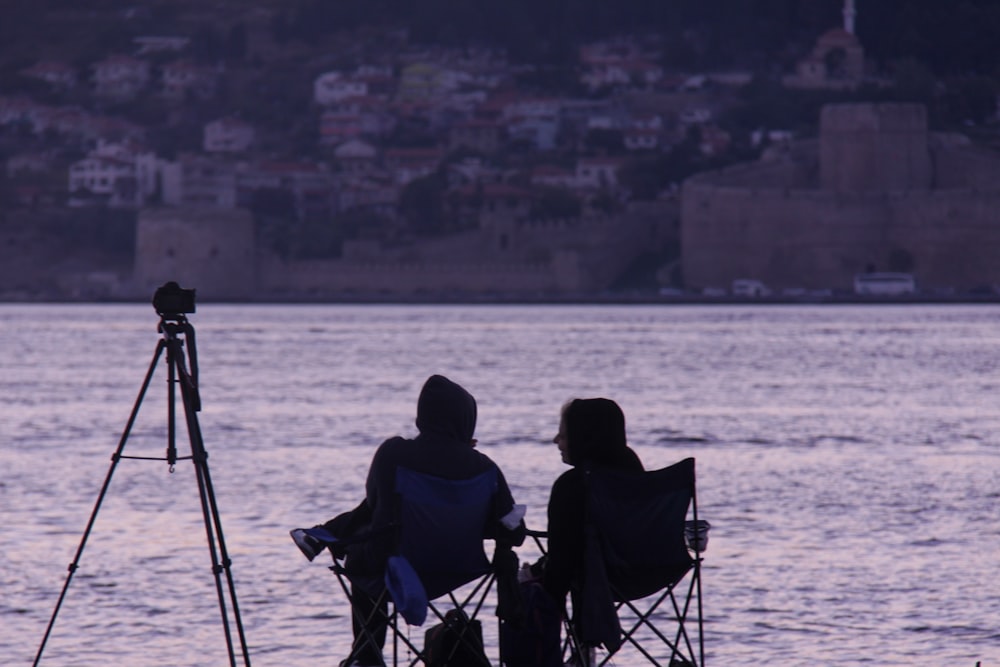 a couple of people sitting in chairs near a body of water