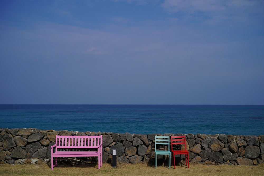 two colorful chairs sitting next to a stone wall