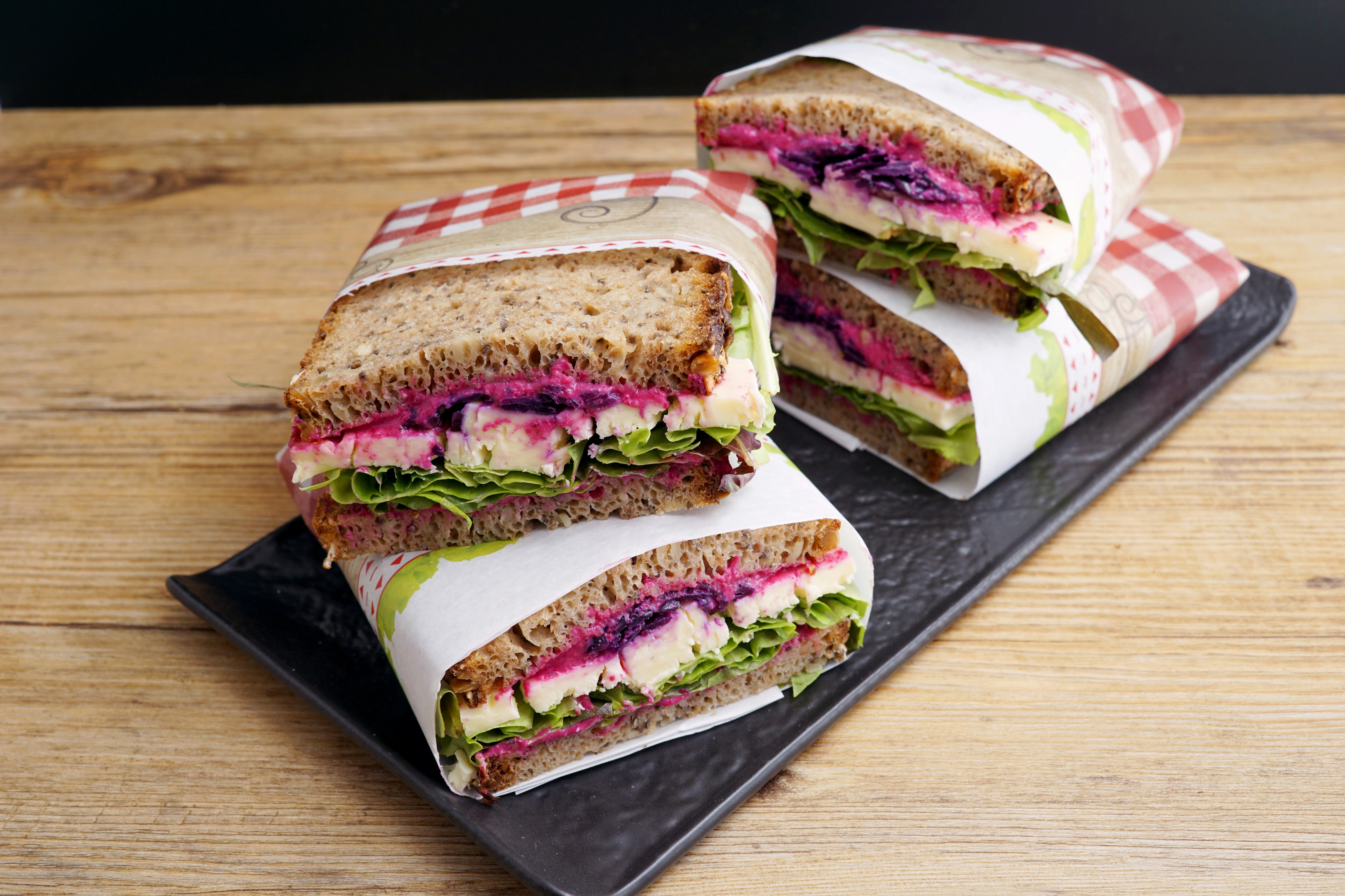 Four delicious looking sandwiches wrapped in paper and resting on a plate.