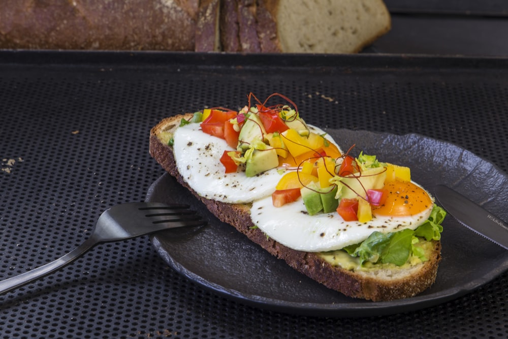 a black plate topped with a piece of bread covered in eggs and veggies