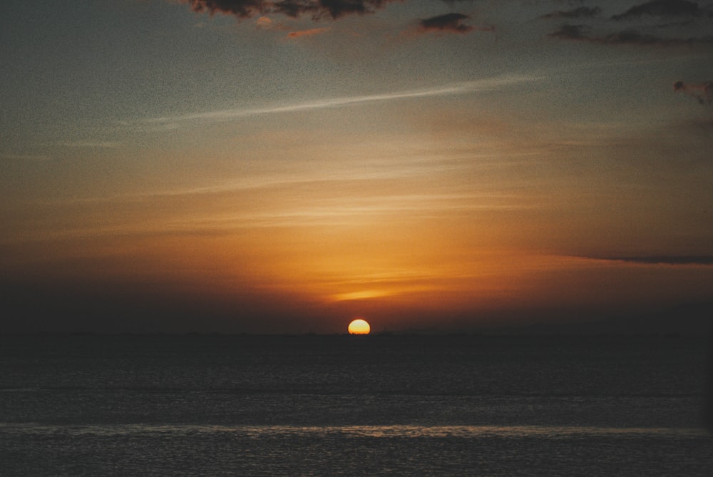 the sun is setting over the ocean on a cloudy day