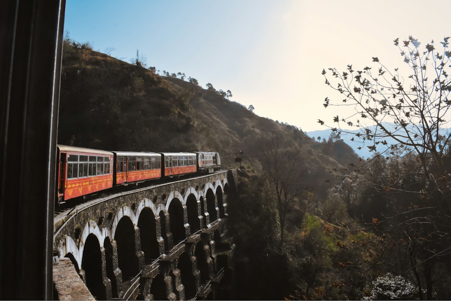 Kalka–Shimla toy train crossing a stone arch bridge on the hillside, seen from a window of the train