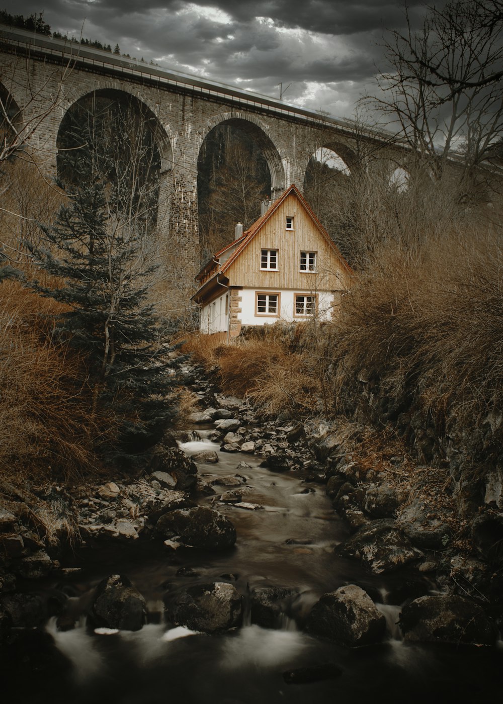 a house sitting on the side of a river next to a bridge