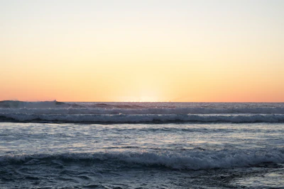 Waves gently crashing on a quiet beach under a pastel-colored sky at sunset