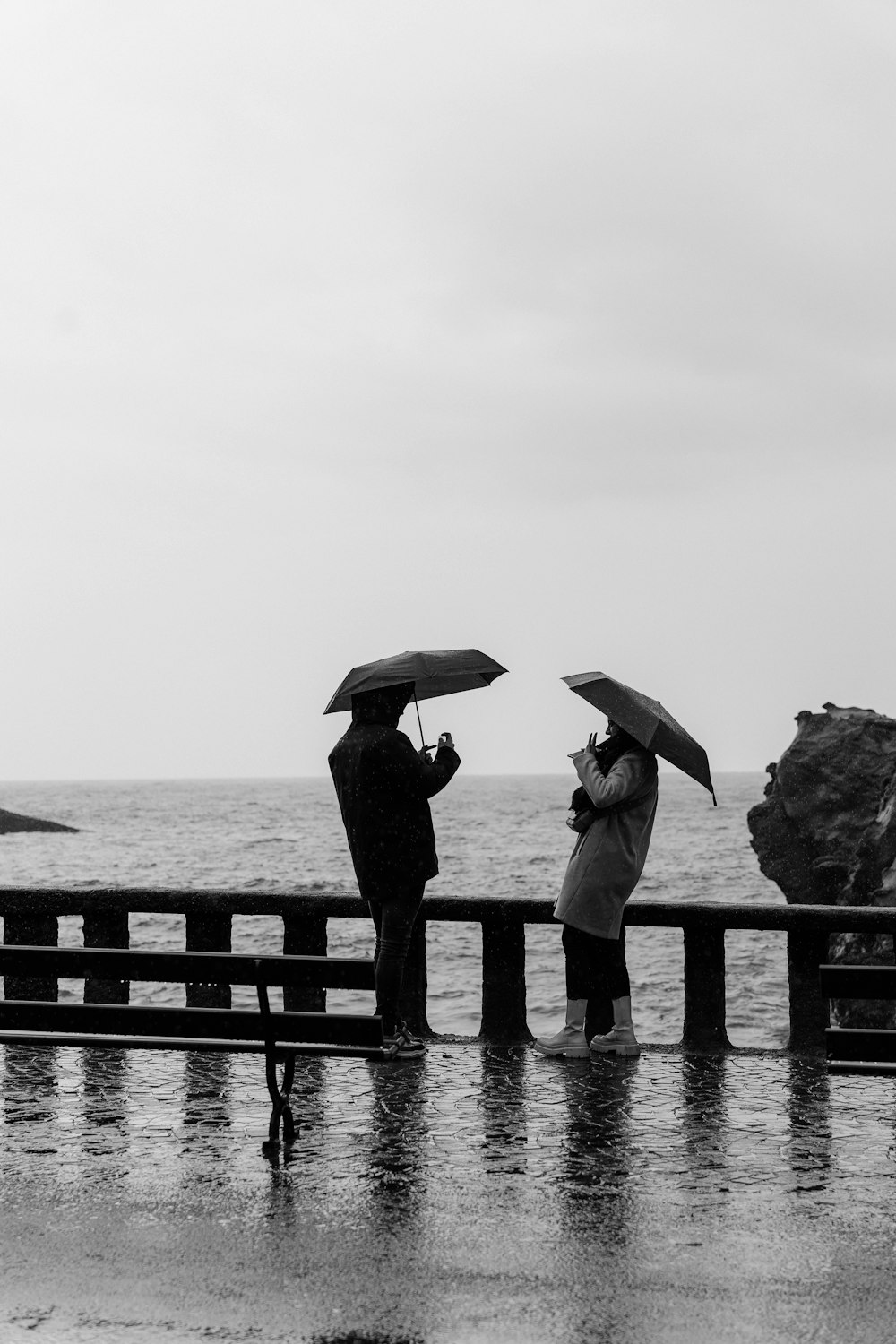 a couple of people standing on a pier holding umbrellas