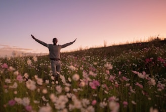a man standing in a field of flowers with his arms outstretched