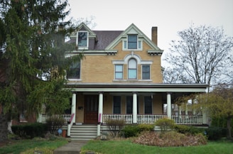 A refurbished historic home with a welcoming porch surrounded by mature trees.