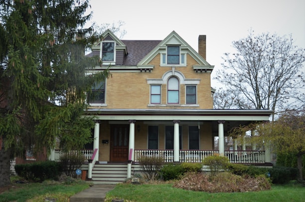 A refurbished historic home with a welcoming porch surrounded by mature trees.