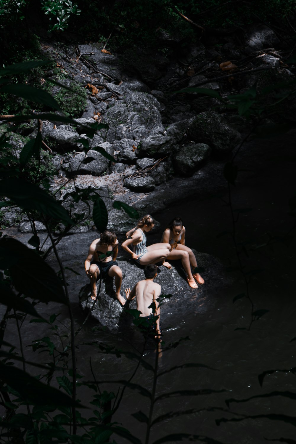 a group of people sitting on top of a rock in a river