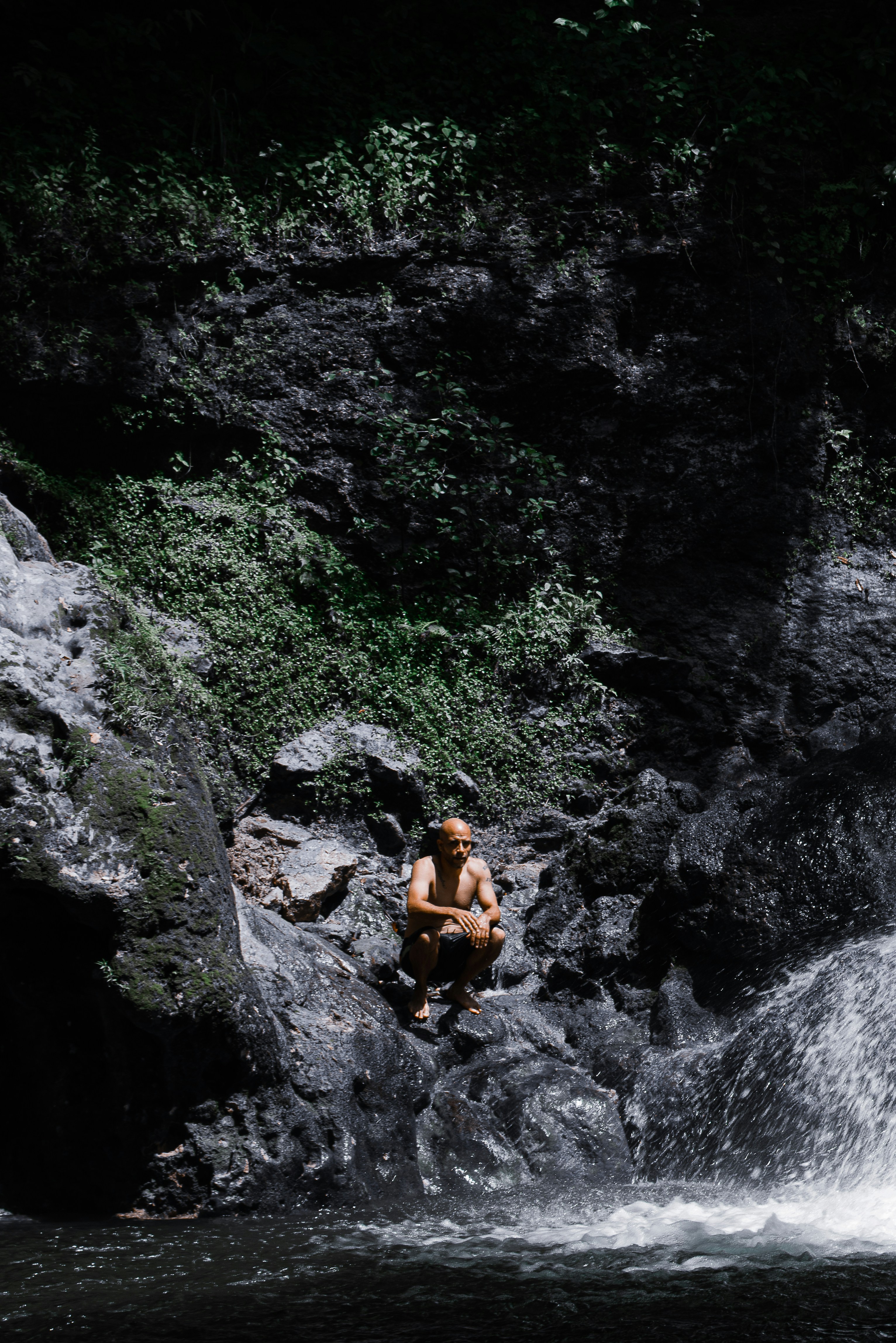 a man sitting on a rock next to a waterfall