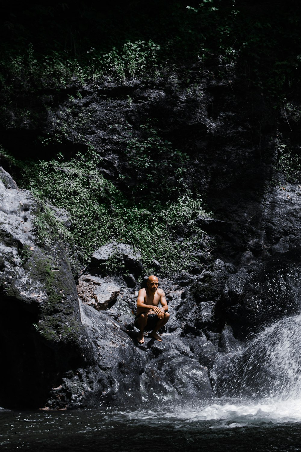 a man sitting on a rock next to a waterfall