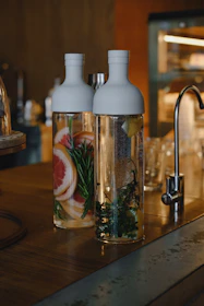 Bottles of alkaline and hydrogenated water with fresh herbs and honeycomb nearby.