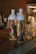 Two glass bottles filled with water are placed on a wooden counter. One bottle contains slices of grapefruit and sprigs of rosemary, while the other contains lemon slices and leafy herbs. The setting appears to be a kitchen or bar area with a metallic faucet in the background.