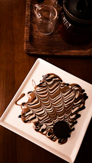 Hands elegantly plating a matcha dessert next to a Godiva chocolate centerpiece, capturing the blend of flavors.