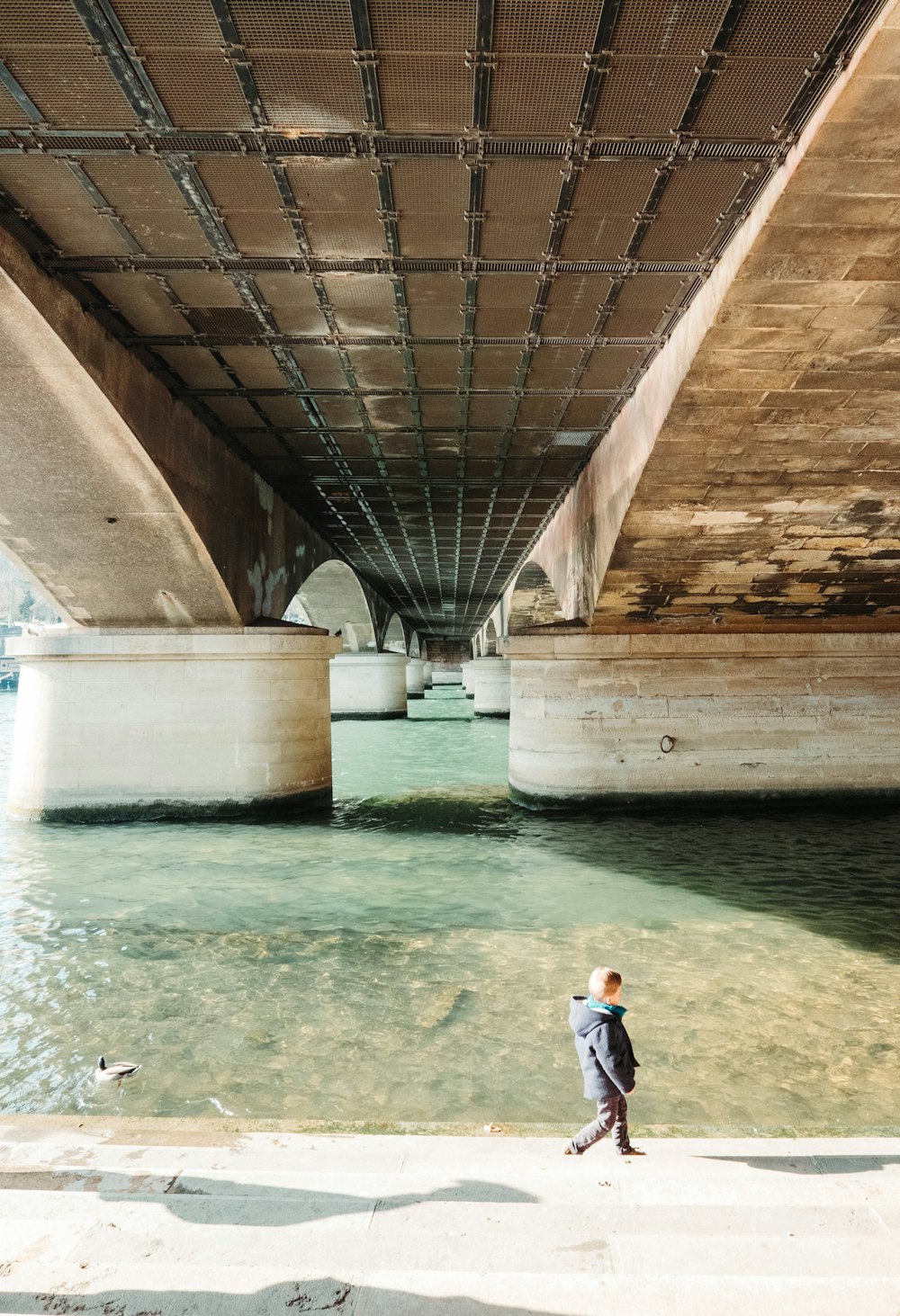 um homem andando sob uma ponte ao lado de um corpo de água