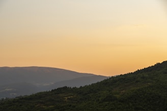 A serene landscape featuring two distant green hills under a warm orange gradient sky, symbolizing hope and new beginnings.