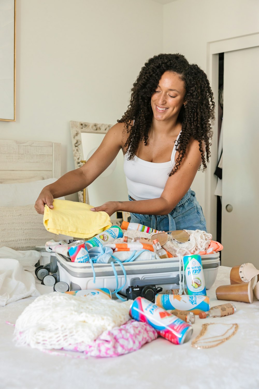 a woman standing over a bed with a suitcase full of items