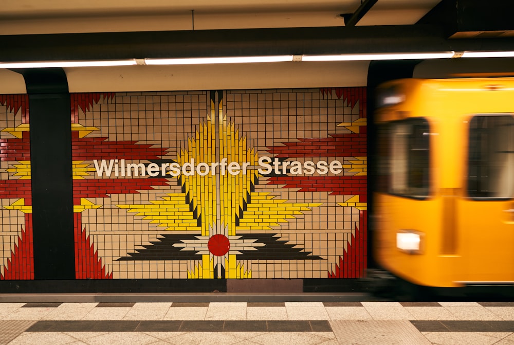 un train jaune passant devant un mur avec une photo dessus