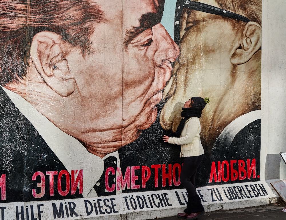 Una mujer parada frente a una pintura de un hombre besando a otro hombre
