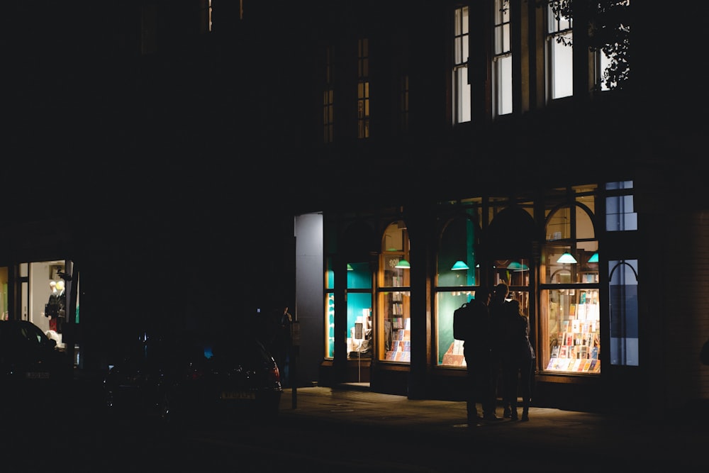 a couple of people standing outside of a building at night