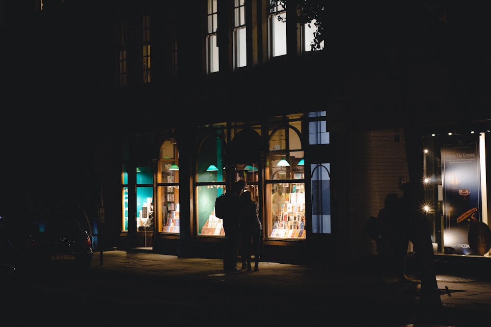 a couple of people standing outside of a building at night