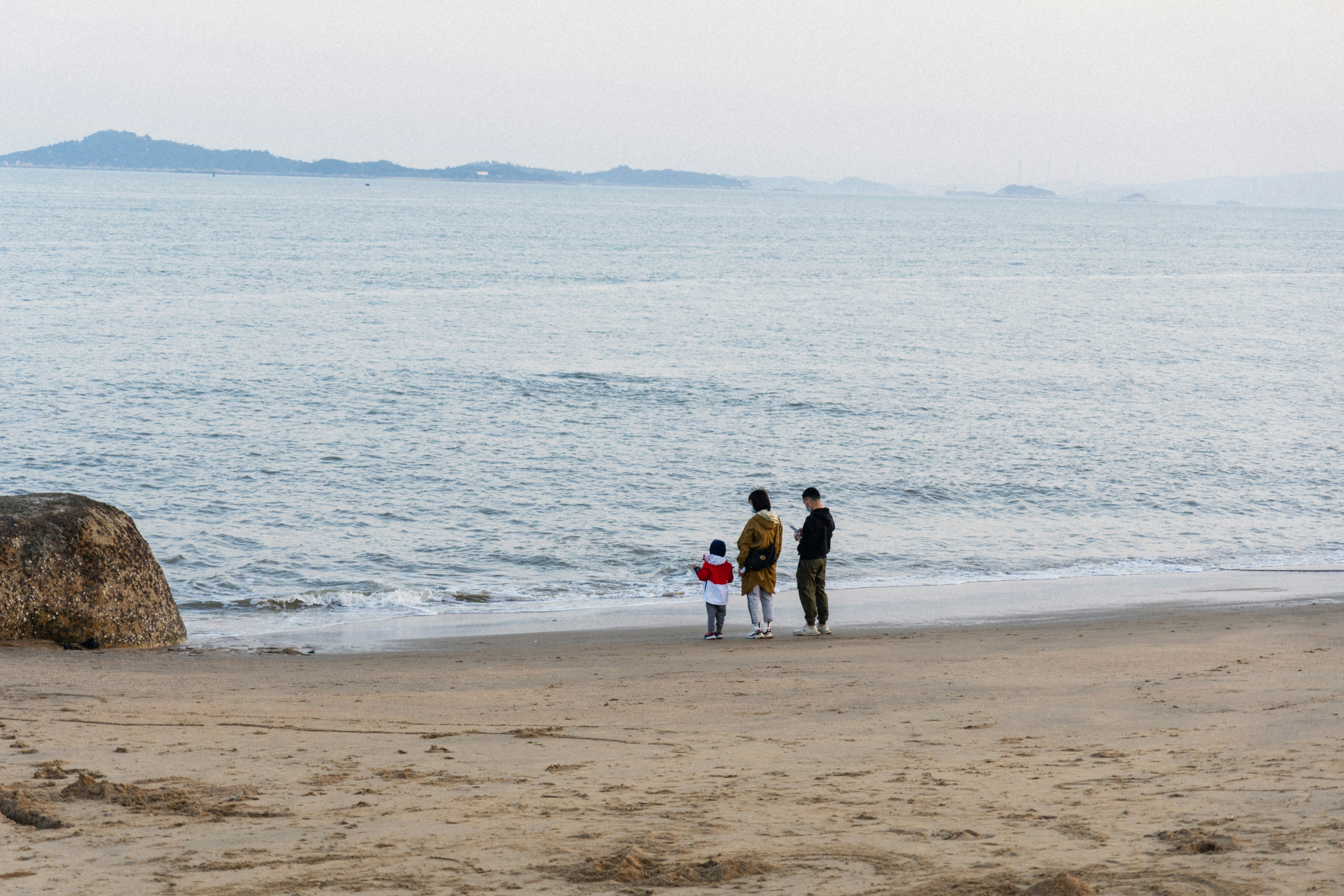 a family of three standing on a beach next to the ocean