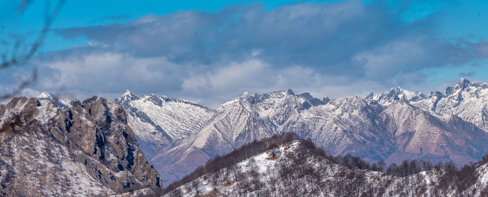 a snowy mountain range under a cloudy blue sky