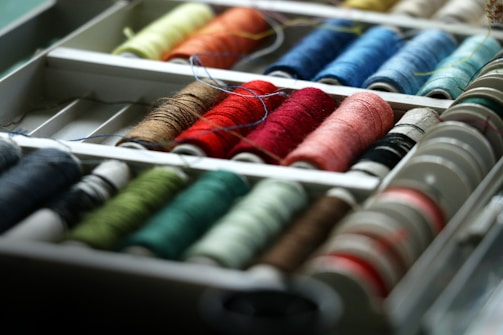 Rows of colorful spools of thread arranged in a compartmentalized container, showcasing a variety of hues and textures.