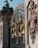 Ornate iron gates with intricate golden embellishments. The design includes detailed sculptures and decorative patterns. Stone structures with elaborate carvings flank the gates, depicting various symbols and figures.