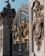 Ornate iron gates with intricate golden embellishments. The design includes detailed sculptures and decorative patterns. Stone structures with elaborate carvings flank the gates, depicting various symbols and figures.