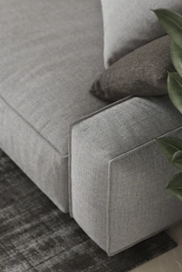 A sleek modern sofa in soft gray fabric shown in a detailed 3D view highlighting its clean lines and plush cushions.