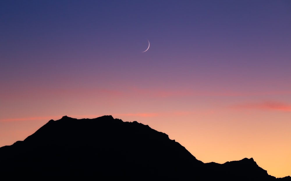 the moon is setting over a mountain in the sky