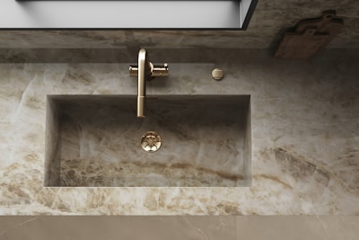 A marble bathroom sink with a sleek, modern design features a metallic faucet. The surrounding countertop and backsplash are made of the same marble material, complementing the overall minimalist aesthetic. A wooden cutting board is placed on the right side of the counter.