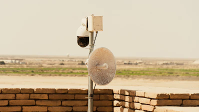A solar-powered CCTV camera mounted on a sunny wall overlooking a garden.