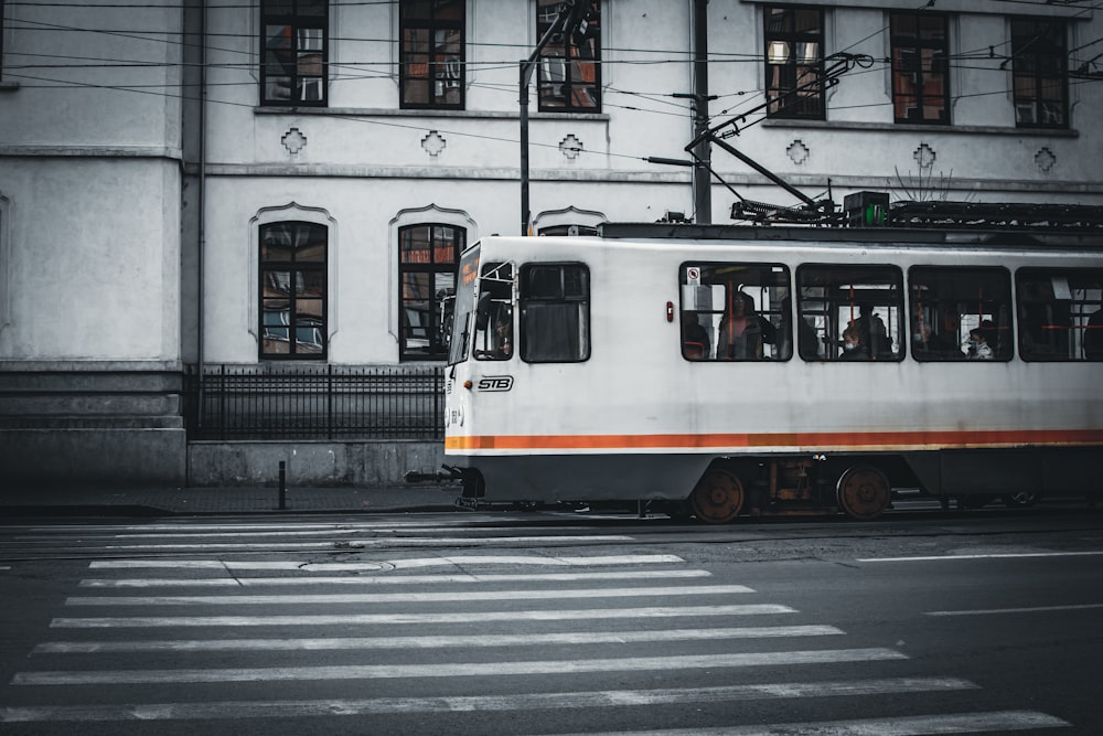 a white and orange train traveling past a tall building