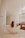 A modern bathroom features a sleek, freestanding bathtub with a person relaxing inside, their long hair cascading over the tub's edge. The room is elegantly designed with neutral tones, wooden cabinet drawers filled with neatly stacked towels, and a large wall mirror. A glass shower stall is positioned next to the bathtub, and soft lighting adds a warm ambiance.