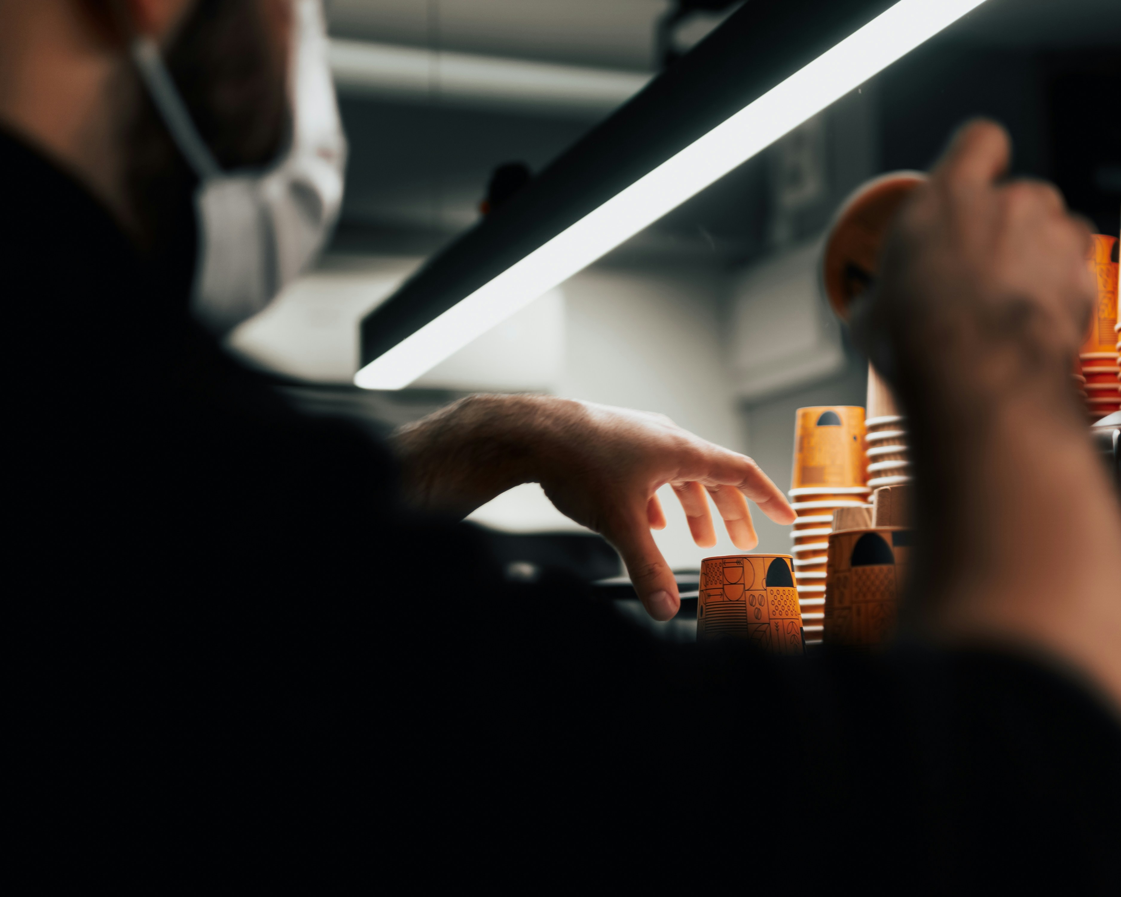 Barista in a mask reaching for takeaway cups behind a counter