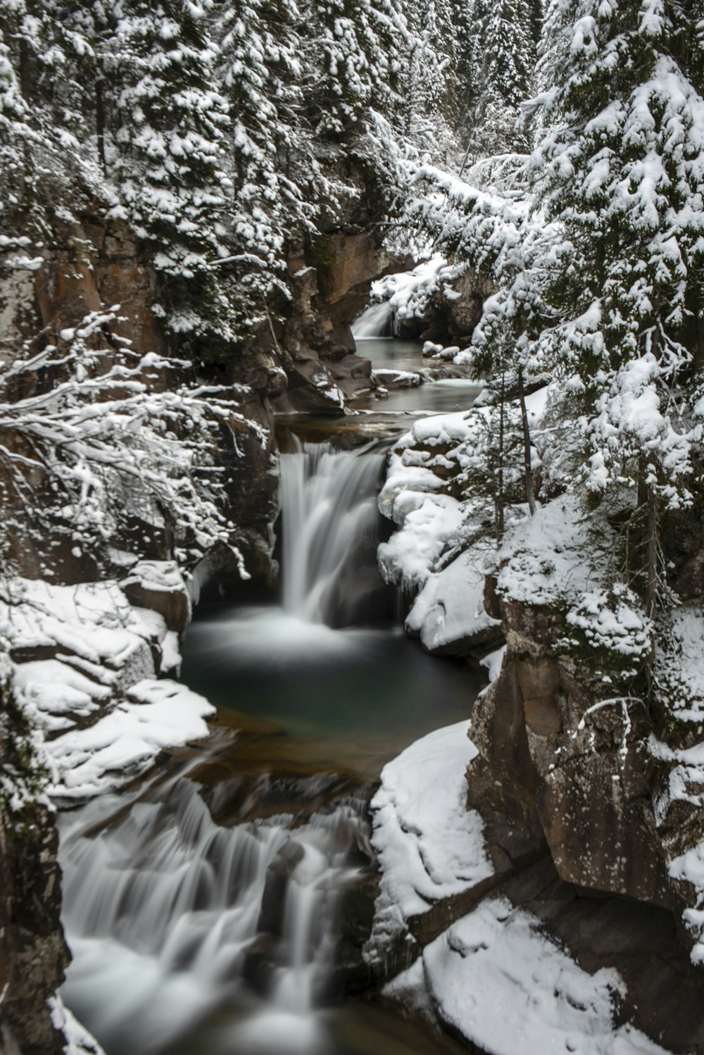 a small waterfall surrounded by snow covered trees