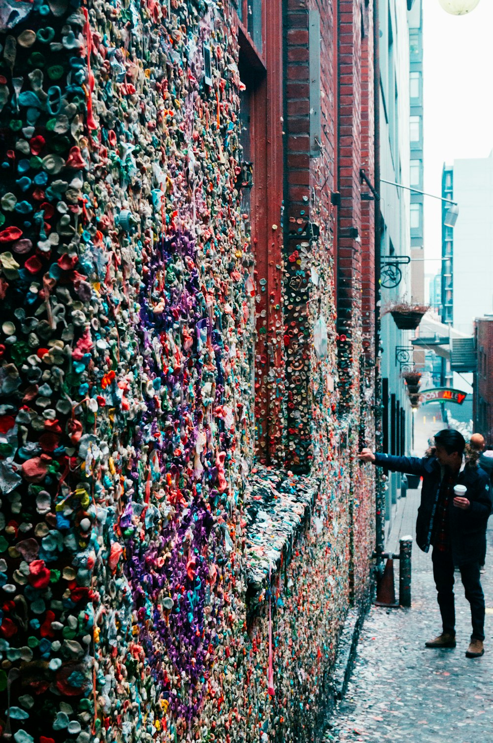 a couple of people walking down a street next to a wall covered in lots of