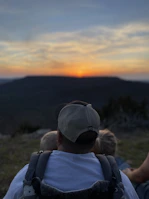 Parents and children sitting quietly on a porch, watching a soft sunset over rolling hills.