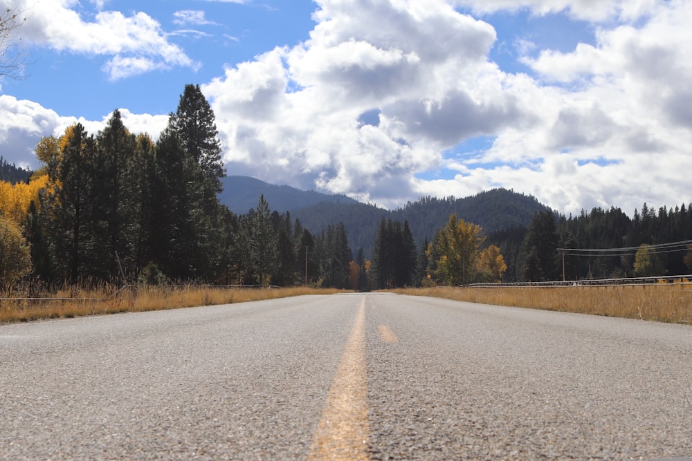 an empty road with trees and mountains in the background