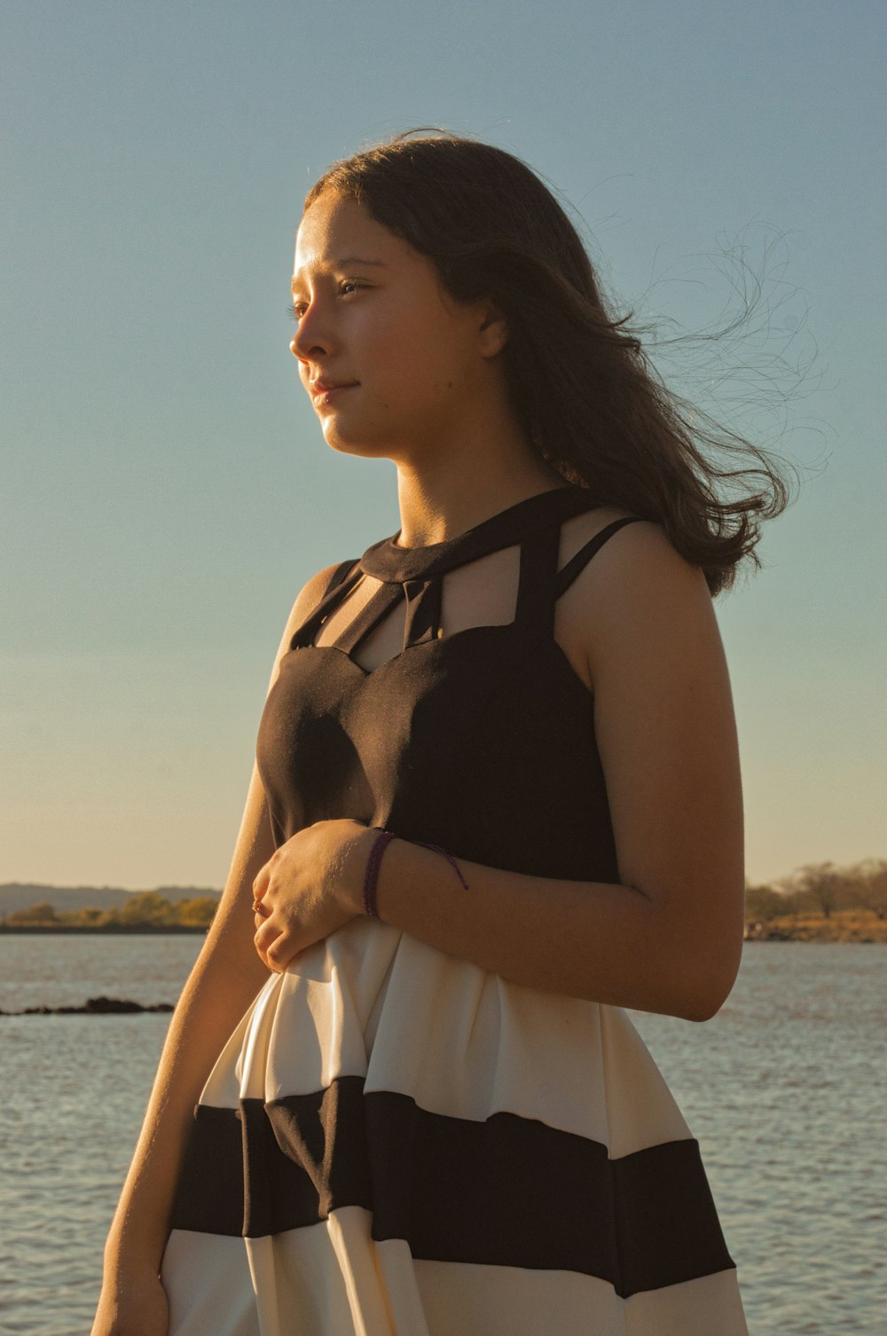 a woman in a black and white dress standing by a body of water