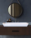 A sleek decorative mirror hanging above a modern sink with soft lighting.