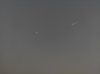 A night sky featuring a bright star or planet on the left and a meteor streaking across on the right against a dark, clear background.