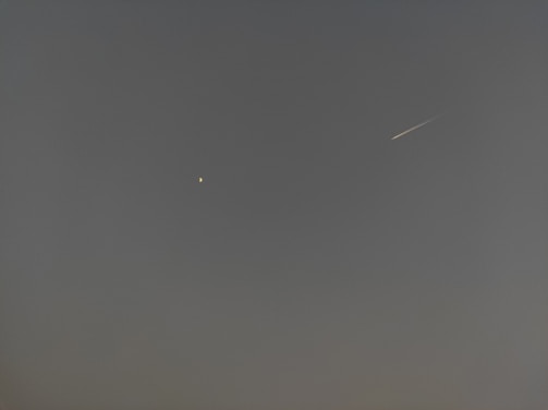 A night sky featuring a bright star or planet on the left and a meteor streaking across on the right against a dark, clear background.