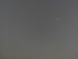 A night sky featuring a bright star or planet on the left and a meteor streaking across on the right against a dark, clear background.