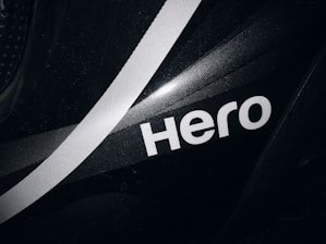 A close-up view of a black surface featuring a bold, white, stylized word 'Hero' with a white diagonal stripe running through the background. The surface has a subtle texture and glossy finish.