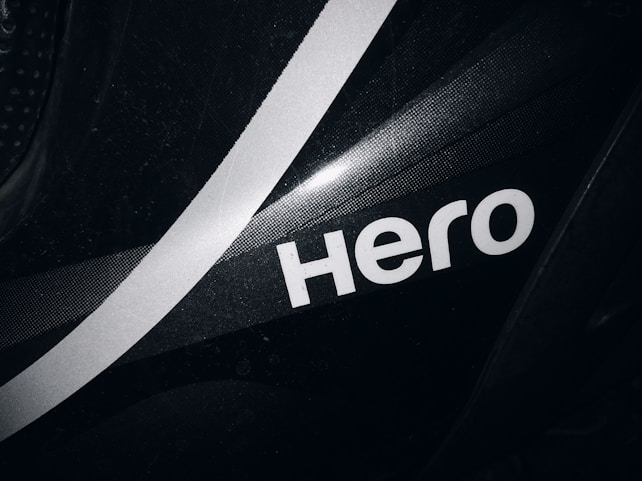 A close-up view of a black surface featuring a bold, white, stylized word 'Hero' with a white diagonal stripe running through the background. The surface has a subtle texture and glossy finish.